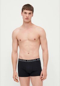 Boxers pretos com uma cintura elástica à venda. O tecido parece liso e ajustado, destacando a fisionomia do modelo.