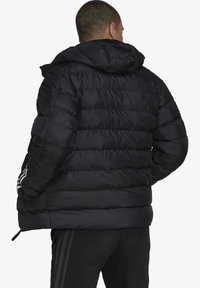 Sort pufferjakke med hætte, med en quiltet design, elastiske manchetter og tre hvide striber på hver ærme.