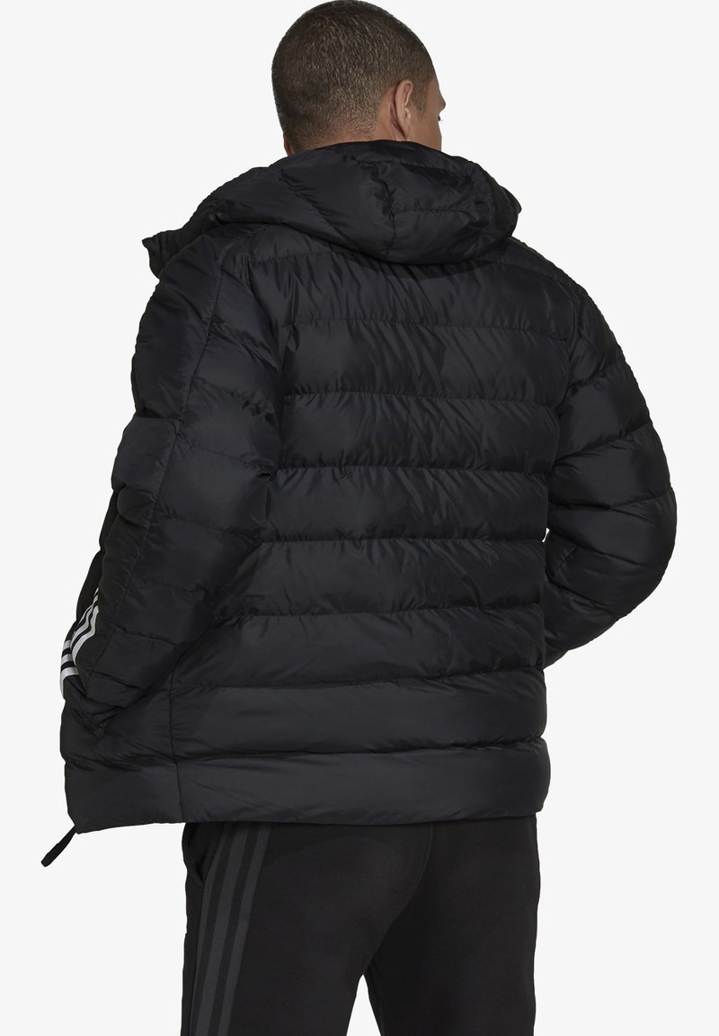 Sort pufferjakke med hætte, med en quiltet design, elastiske manchetter og tre hvide striber på hver ærme.