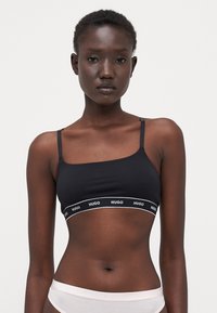 Bralette en coton noir avec de fines bretelles et une bande élastique à logo arborant "HUGO" en blanc. Design simple et sans coutures, idéal pour le superposition.