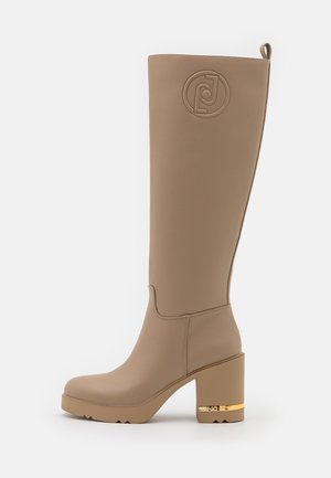 Hoher Stiefel aus taupefarbenem Leder mit Blockabsatz, geprägt mit einem runden Logo nahe dem oberen Rand, mit einem Zugriemen und goldfarbener Applikation am Absatz.