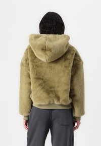 Olive roheline faux fur kapuutsiga, millel on struktureeritud lõige, soonikkoes äär ja varrukad ning suur kapuuts. Omab pehmet ja luksuslikku tekstuuri.