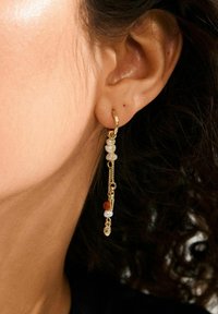 Gouden oorring met een hangende ketting en gekleurde kralen, met een mix van texturen en een verlengde vorm voor extra detail.