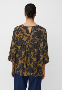 Løst siddende bluse med trekvartærmer i et brunt og sort blomstermønster med blå detaljer. Bagsiden har en nøglehulåbning og knaplukning.