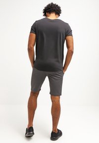 T-shirt noir à manches courtes et short gris, en tissu doux, avec une coupe ajustée. Des chaussures noires complètent la tenue.