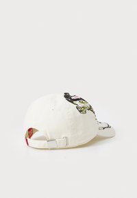 Casquette de baseball en coton crème avec graphique brodé, elle présente une sangle ajustable en boucle argentée et un accent rouge près de l'arrière.