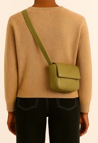 Groene leren crossbodytas met een gestructureerde vorm, met een flap sluiting en een gewatteerd patroon, gedragen over een beige trui en zwarte jeans.