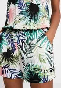 Krátké šortky s potiskem tropických listů, elasticitním pasem a bočními kapsami, nošené s odpovídajícím topem na tmavé pleti.