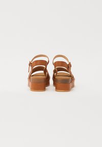 Brune lærsandaler med åpen bakdesign, justerbar ankelreim og en tykk plattformsåle. Glatt tekstur med minimal detaljering.