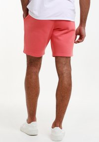 Pantalones cortos de algodón color coral con un diseño simple, que cuentan con bolsillos laterales, una textura suave y dobladillos enrollados. Combinados con zapatillas blancas.
