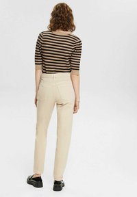 Gestreepte zwart en beige trui met korte mouwen, gecombineerd met beige slim-fit broek en zwarte schoenen, gezien van achteren.