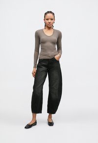 Dlhý rukáv, priliehavý top v taupe farbe, kombinovaný s čiernymi džínsami s vysokým pásom a širokými nohavicami a čiernymi balerínkami, s jednoduchým dizajnom a textúrovanou látkou.