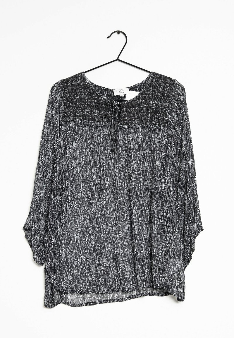 Blouse à manches longues à motif noir et blanc avec encolure ronde et détail à nouer, suspendue à un cintre noir sur fond blanc.