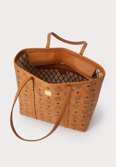 Tan tote bag with vertical shape, smooth leather handles, perforated lining, and a patterned exterior featuring brand logos and diamond shapes.