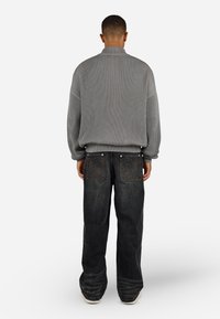 Grå ribbestrikket trøje med høj hals, parret med mørke denim jeans, der har dekorativ syning på baglommerne og løs pasform.