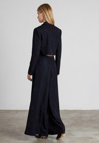 Completo blu navy composto da giacca cropped e pantaloni a gamba larga con righe verticali e sottili dettagli scintillanti. Texture liscia.
