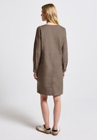 Braunes Leinenkleid mit langen Ärmeln, geradem Schnitt und schmalem Saum. getragen mit lässigen Turnschuhen, zeigt eine einfache Rückansicht.