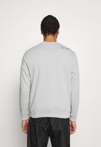 Grå sweatshirt med rund hals och långa ärmar. Nike-logotyp i blått på övre delen av ryggen. Slät textur och avslappnad design.