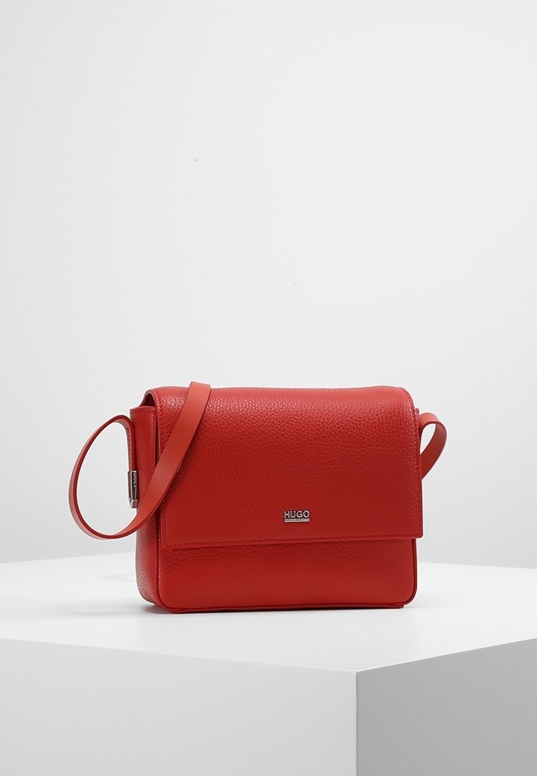 Rød læder crossbody taske med tekstureret overflade, rektangulær form, klaplukning og justerbar rem. Har et mærket logo på fronten.