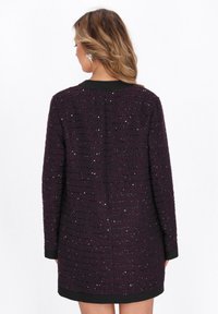 Violetti teksturoitu mekko mustalla kauluksella, jossa on vaakasuoria raitoja ja hienovaraisia paljetteja. Keskipitkä, pitkät hihat ja suora leikkaus.