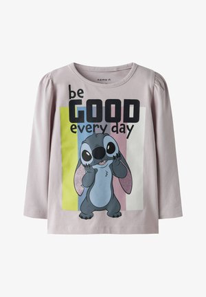 Chemise à manches longues en tissu rose clair présentant un personnage de dessin animé aux grands yeux, détails scintillants, et le texte « sois BON chaque jour ».