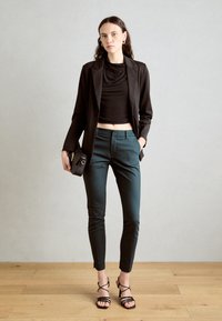 Černý blejzr přes černý cropped top, doplněný úzkými tepláky v barvě modrozelené. Doplněno malou černou kabelkou a černými sandály na podpatku.