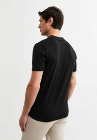 Zwarte korte mouw gebreide trui met een ronde hals en geribbelde zoom. De stof lijkt glad en aansluitend. De broek is beige.