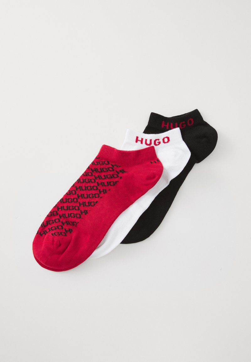 Trys poros žemų kojinių raudonos, baltos ir juodos spalvų, kiekviena su "HUGO" prekės ženklu; raudonoji pora turi pakartotinius juodus logotipus.