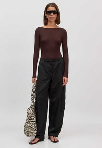 Bruine langarm bodysuit, zwarte cargo broek, zebra-print tas, zwarte slipper en oversized zwarte zonnenbril tegen een neutrale achtergrond.