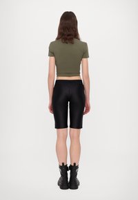 Olivově zelený cropped top, černé lesklé cyklistické šortky a černé kotníkové boty se stříbrnými akcenty. Hladká textura, přiléhavý střih.