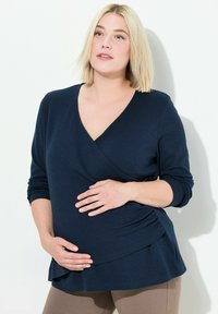 Navyblaues Wickeloberteil mit langen Ärmeln, weichem Material und seitlichen Raffung. Für die Schwangerschaft konzipiert, mit einem V-Ausschnitt und fließender Silhouette.