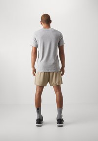 Camiseta de algodón gris combinada con pantalones cortos beige, con un corte relajado. Zapatillas negras y calcetines grises completan el look.
