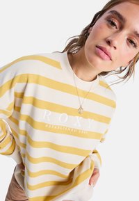 Gelb-weißer gestreifter Sweatshirt mit "ROXY" und "ESTABLISHED 1990" aufgedruckt in Weiß, mit geripptem Kragen und oversized Passform.