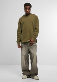 Olīvu zaļš garo piedurknu krekls ar tekstūru, kombinēts ar gaiši pelēkiem plašajiem biksēm un krēmkrāsas sporta apaviem. Vienkāršs dizains, brīvs piegriezums.