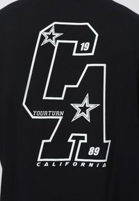 Černé tričko s velkým bílým textem a grafikou. Design zahrnuje "CA", hvězdy a ročníky "19" a "89." Text zní "YOURTURN CALIFORNIA."