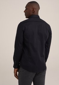 Chemise à manches longues bleu marine avec col pointu et poignets à boutons, au tissu lisse et à la coupe légèrement ajustée.