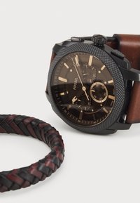 Montre noire avec lunette texturée, bracelet en cuir marron et cadran foncé avec des accents dorés. Comprend un bracelet en cuir tressé noir et bordeaux.
