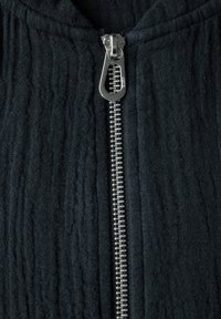 Schwarze Zip-Jacke aus strukturiertem Stoff, mit einem silbernen Metallreißverschluss und Kapuze. Das Material hat ein zerknittertes Aussehen.