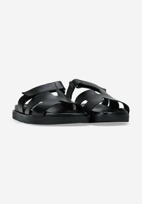 Sandalias negras de cuero suave con diseños troquelados en la parte superior. Suelas planas con una ligera textura para mayor agarre. Estilo minimalista.