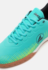 Zapatilla deportiva turquesa con parte superior de tela texturizada, con acentos en negro, seis cordones y un patrón de degradado amarillo cerca de la suela.