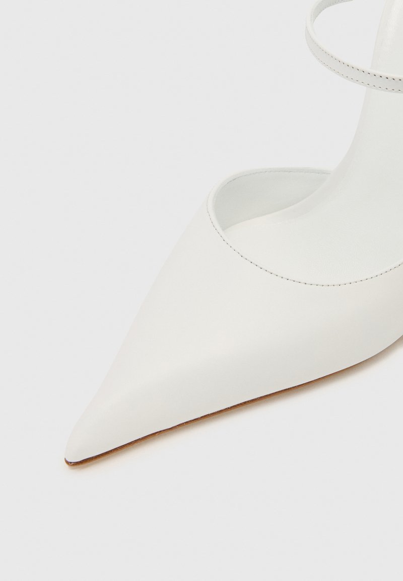Witte leren pump met puntige neus, een gladde afwerking, open zijkanten en een dunne enkelband. De zool heeft een contrasterende tan kleur.