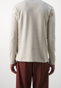 Lichtbeige langemouwen shirt van zachte katoen, met een ronde halslijn en aansluitende manchetten, gecombineerd met donkerrode broeken.