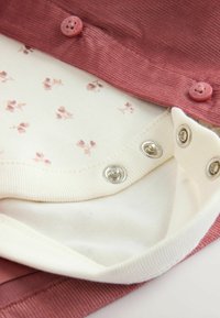 Roze corduroy stoffen shirt met een witte binnenvoering met een klein bloemenpatroon, bevestigd met roze knopen en zilveren drukknoopjes.