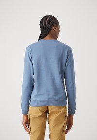 Blaues Sweatshirt mit geripptem Rundhalsausschnitt und Bündchen, mit einer glatten Textur. Die Rückseite ist schlicht und wird durch beigefarbene Cargo-Hosen ergänzt.