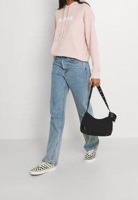 Ljust rosa hoodies med vit text, blå denimjeans, svart väska med nitar på remmen och rutiga slip-on skor.