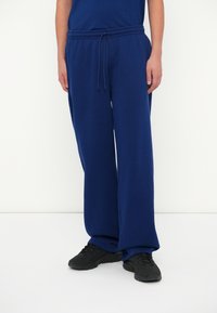 Marineblauwe joggingsbroek met een relaxte pasvorm, koordsluiting en zacht, gestructureerd materiaal. Gepaard met zwarte sportschoenen.