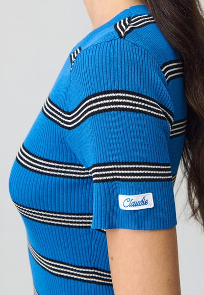 Maglione azzurro a coste con righe orizzontali bianche e nere. Presenta maniche corte e un'etichetta bianca con la scritta "Claudie" sulla manica.