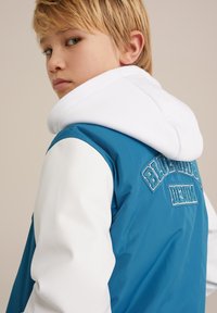 Modrá a biela kapucňová bunda s hladkou textúrou, na zadnej strane s vyšitým detailom "BLUE RIDGE DENIM".