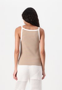Brunstripet tanktop med hvite detaljer, med ribbestruktur. Kombinert med hvite, strikkede, løse bukser.