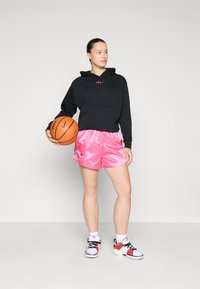 Hanorac negru cu buzunar frontal și logo roz, pantaloni scurți de baschet strălucitori roz și adidași sport negri, roșii și albi, ținând o minge de baschet.